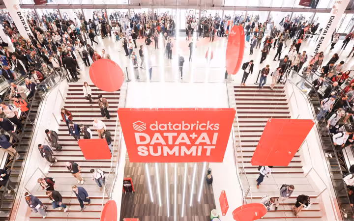 Crowds fill staircases around Databricks Data+AI Summit signs in a bright hall.