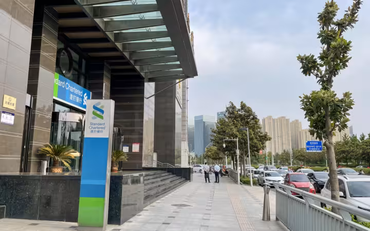 Standard Chartered Zhengzhou Branch sign outside a modern building beside parked cars