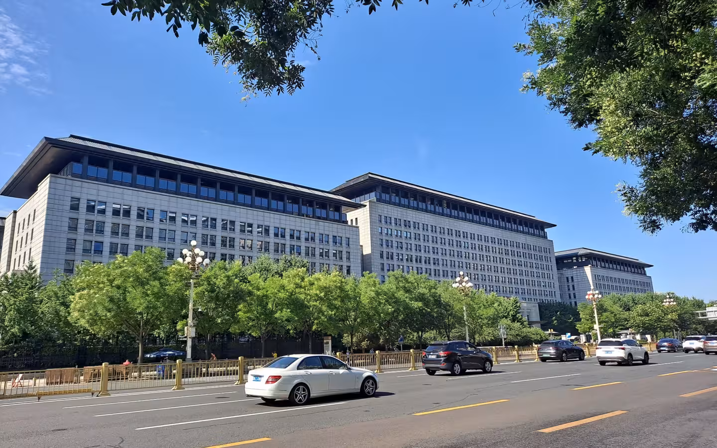 Ministry of Commerce buildings behind roadside trees and passing cars in Beijing