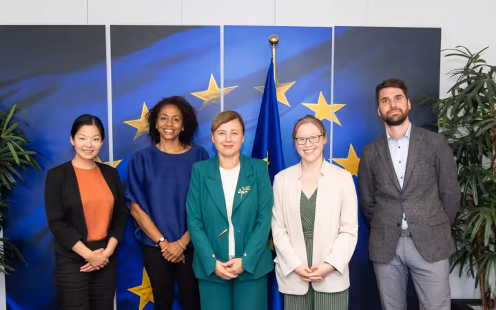 Five people pose before European Union flag panels during an OpenAI visit.