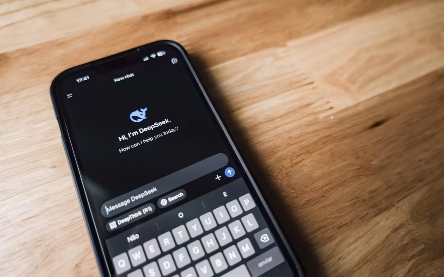 A smartphone displaying DeepSeek's chat interface lies on a wooden table.