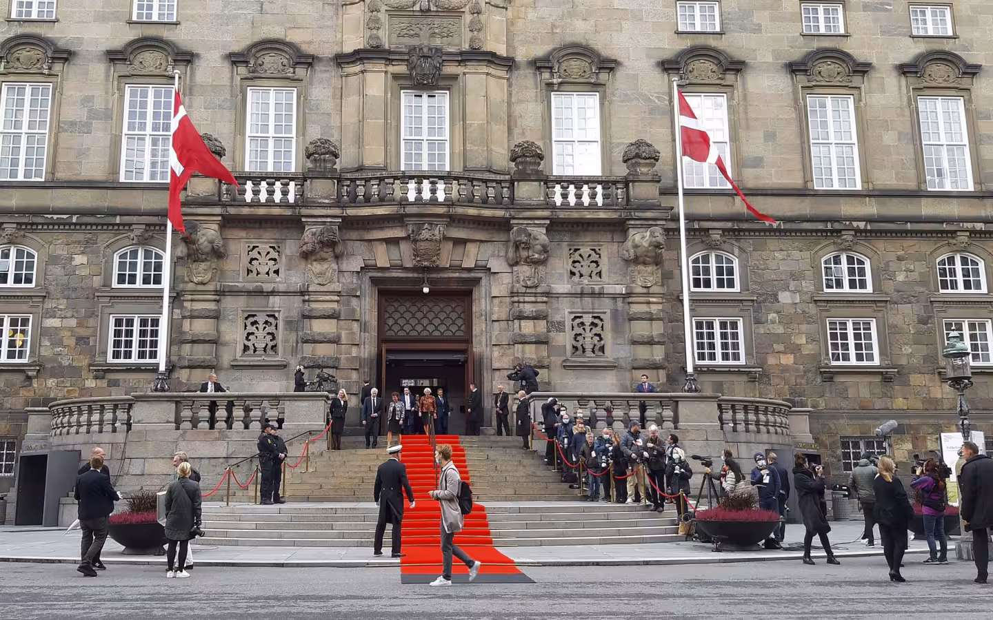 Folketinget's stone facade, Danish flags, a red carpet and people on the steps