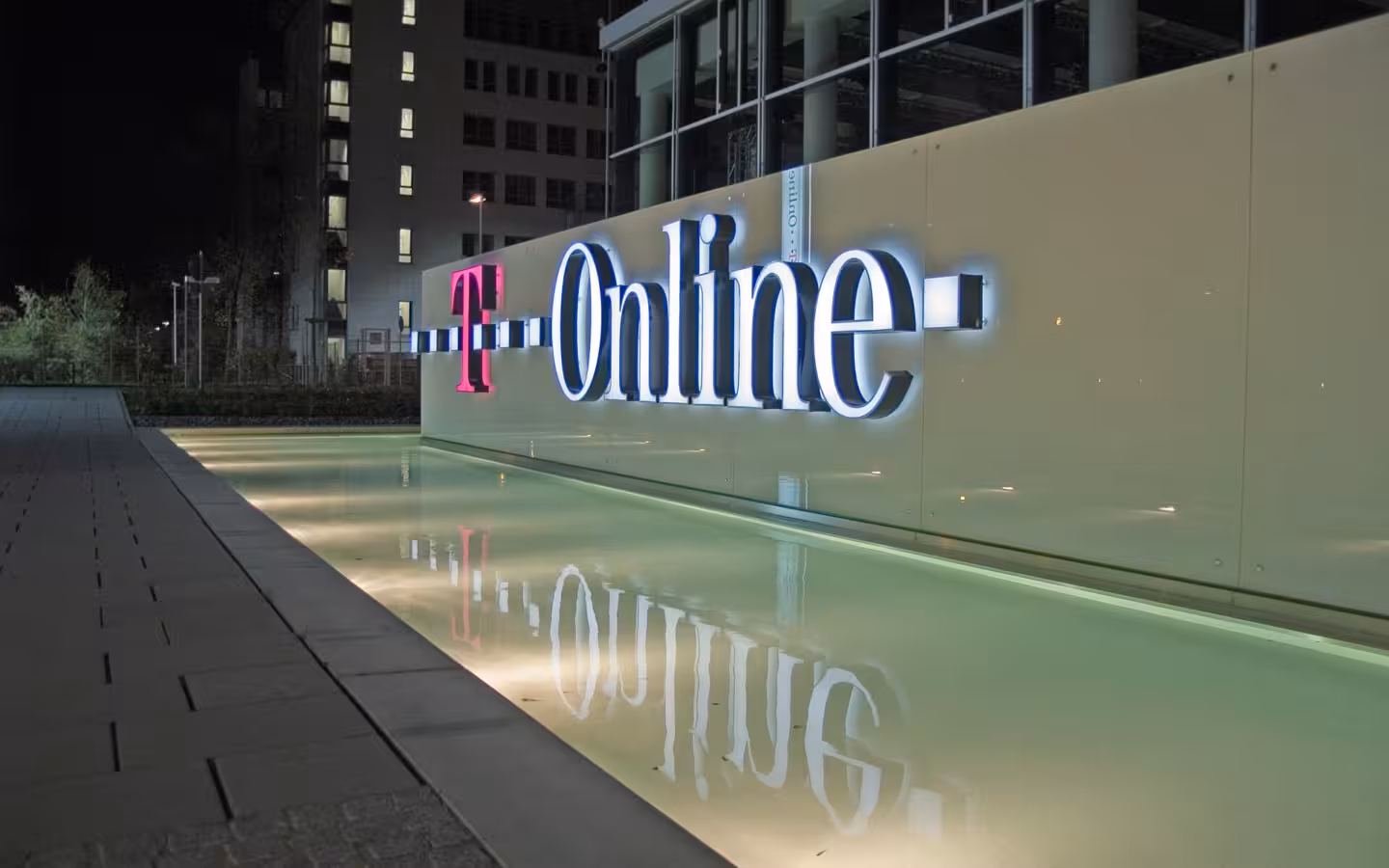 Illuminated T-Online headquarters sign reflects in water outside Darmstadt offices at night