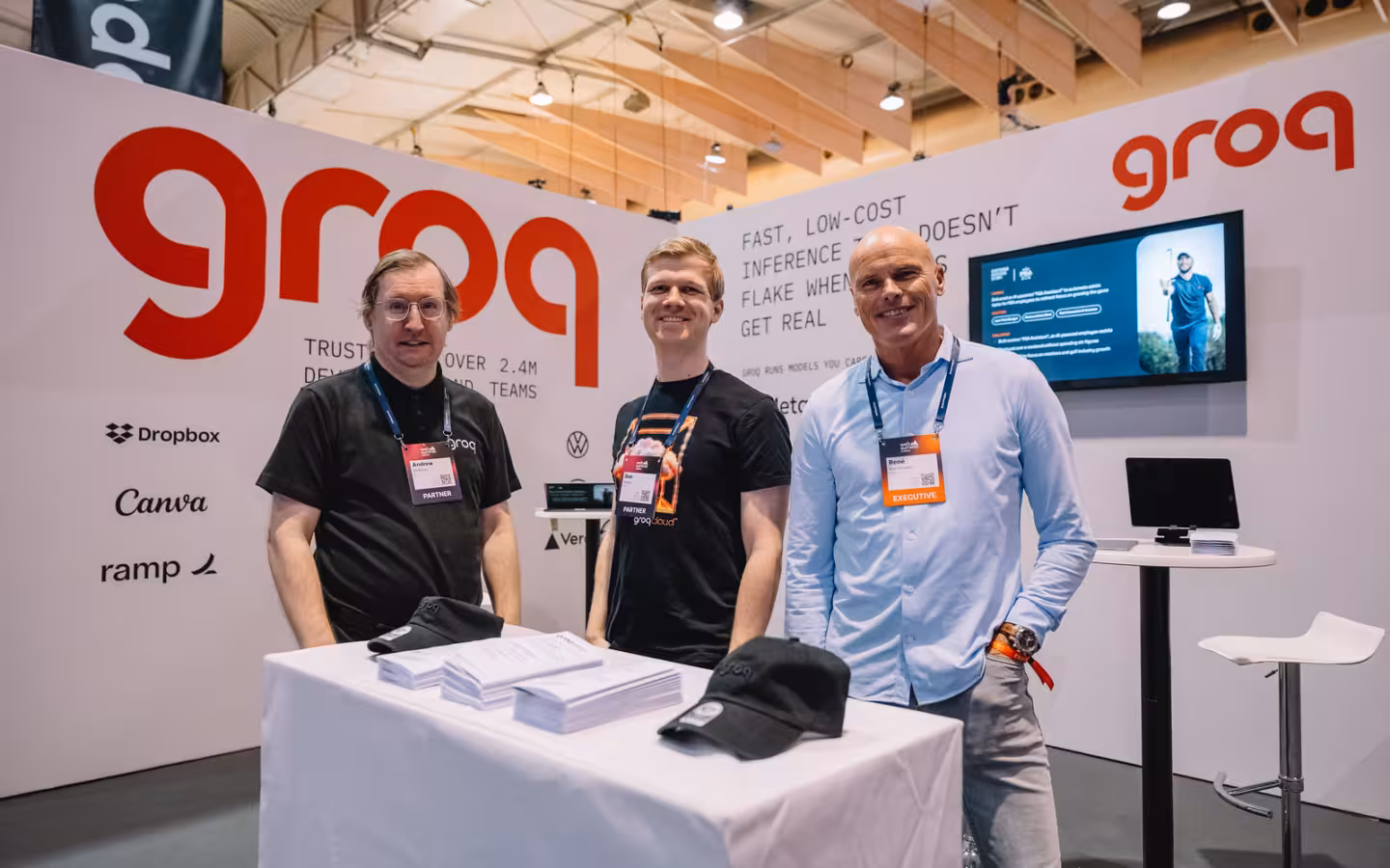 Three people stand behind a table at a Groq exhibition booth.
