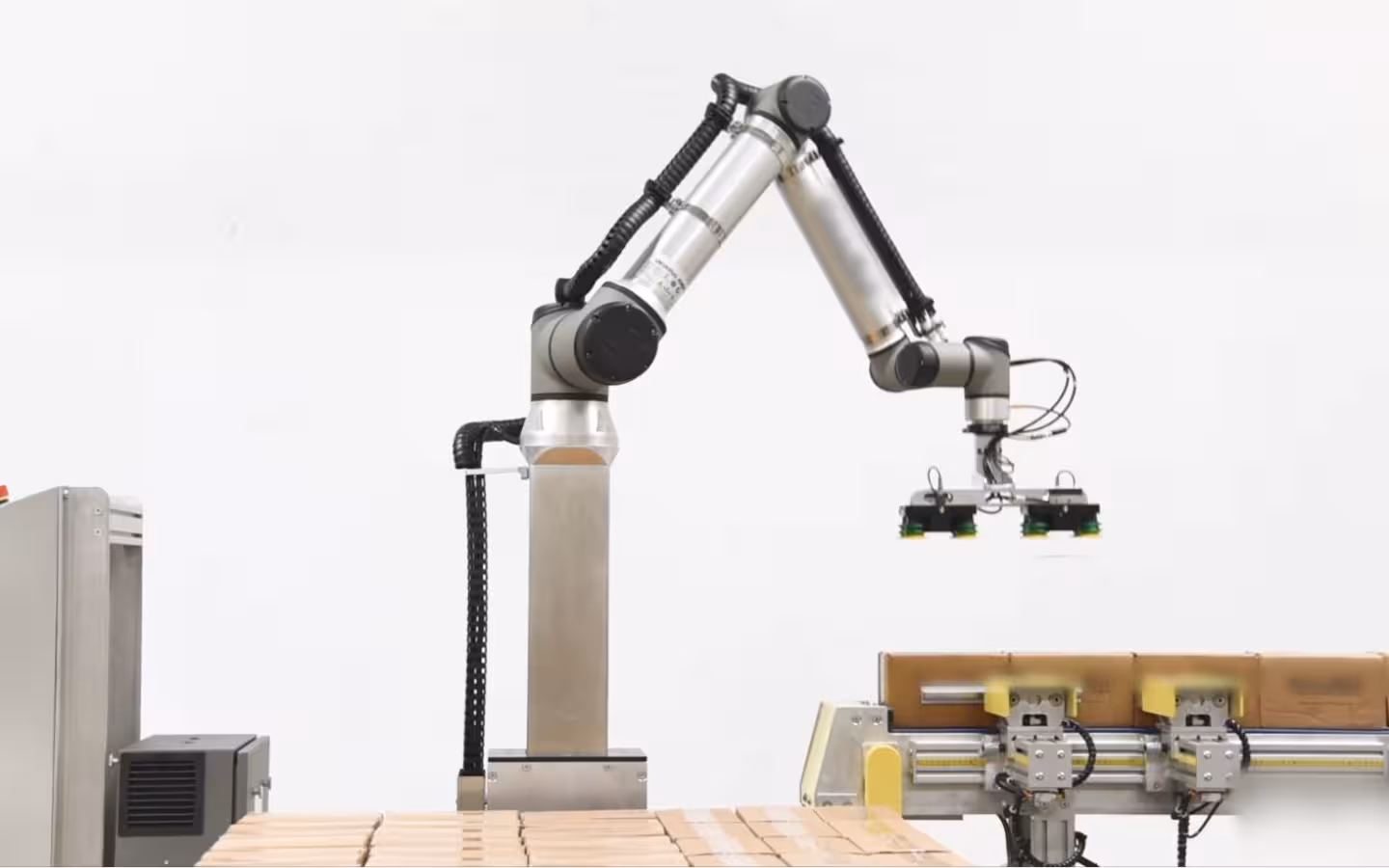 A collaborative robotic arm hovers over boxes on a palletizing line.