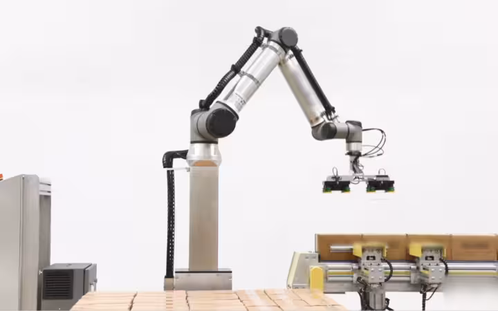 A collaborative robotic arm hovers over boxes on a palletizing line.