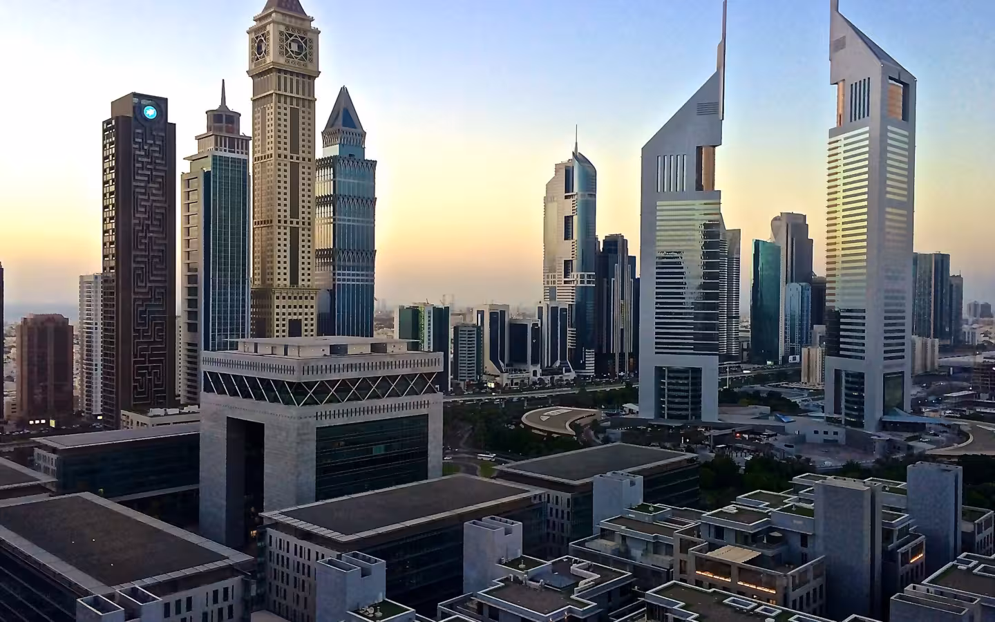 Emirates Towers rise above Dubai’s skyline at dawn, with rooftops in the foreground.