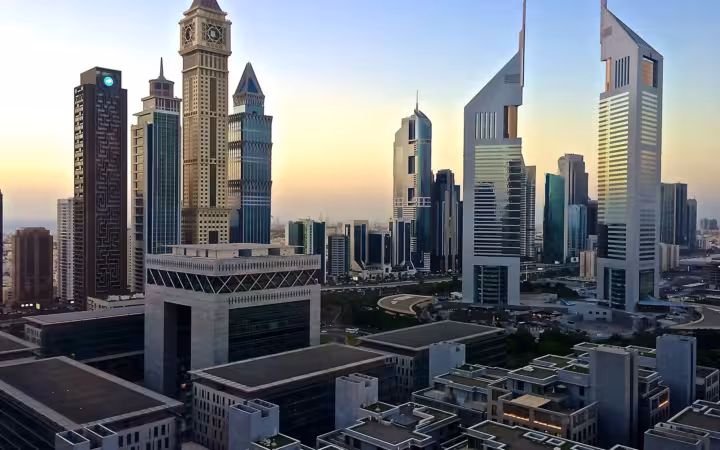 Emirates Towers rise above Dubai’s skyline at dawn, with rooftops in the foreground.