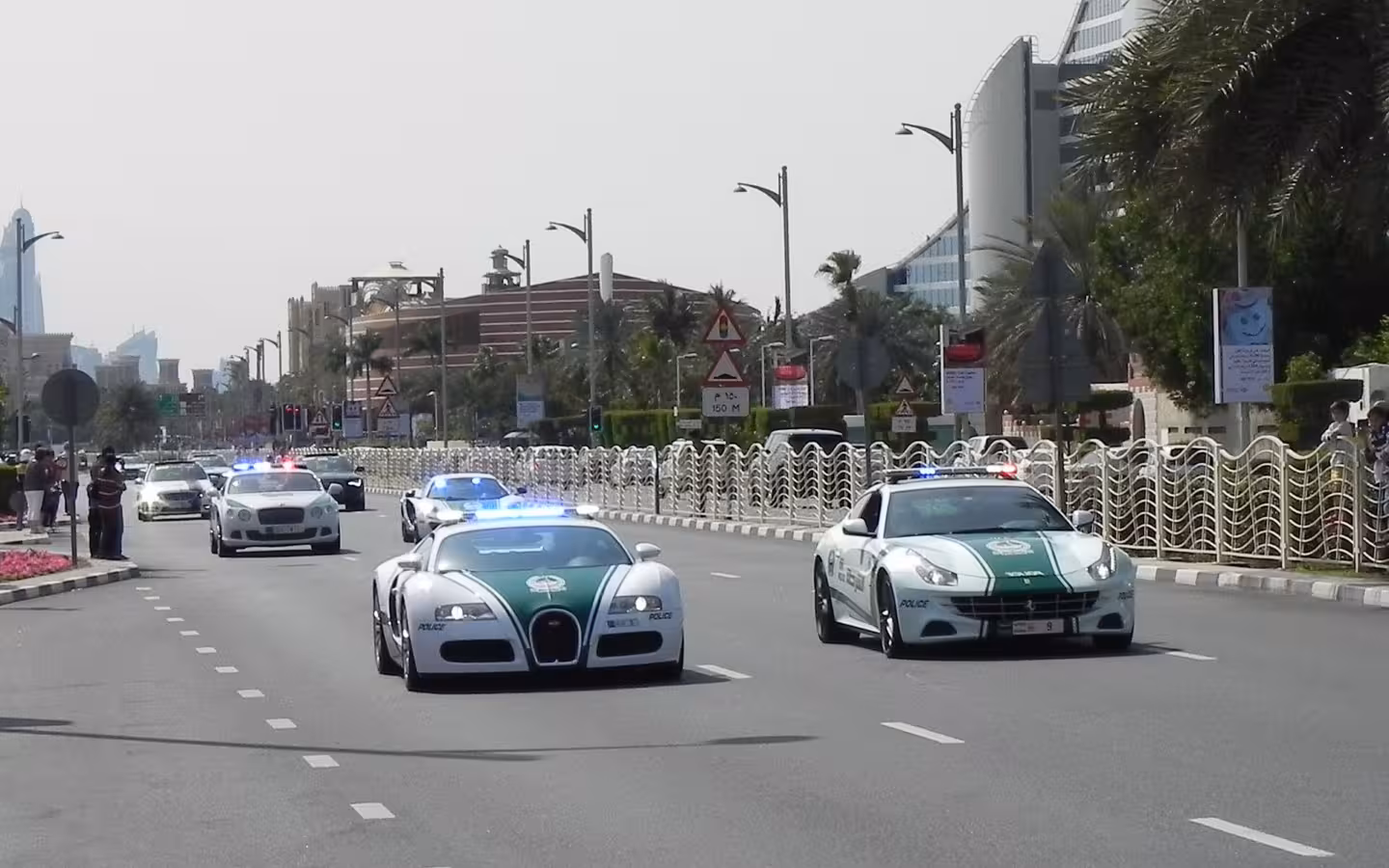 Several Dubai Police sports cars drive along a sunlit city road.