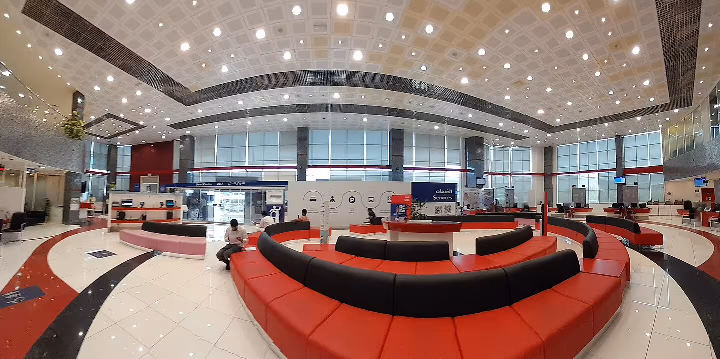 Wide-angle interior view of a modern customer service waiting room with red seating.