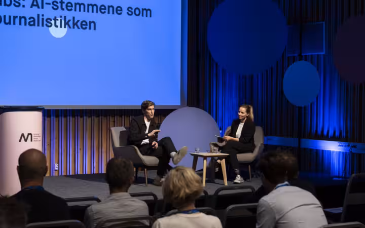 Two speakers discuss AI voices onstage before an audience at NMD.
