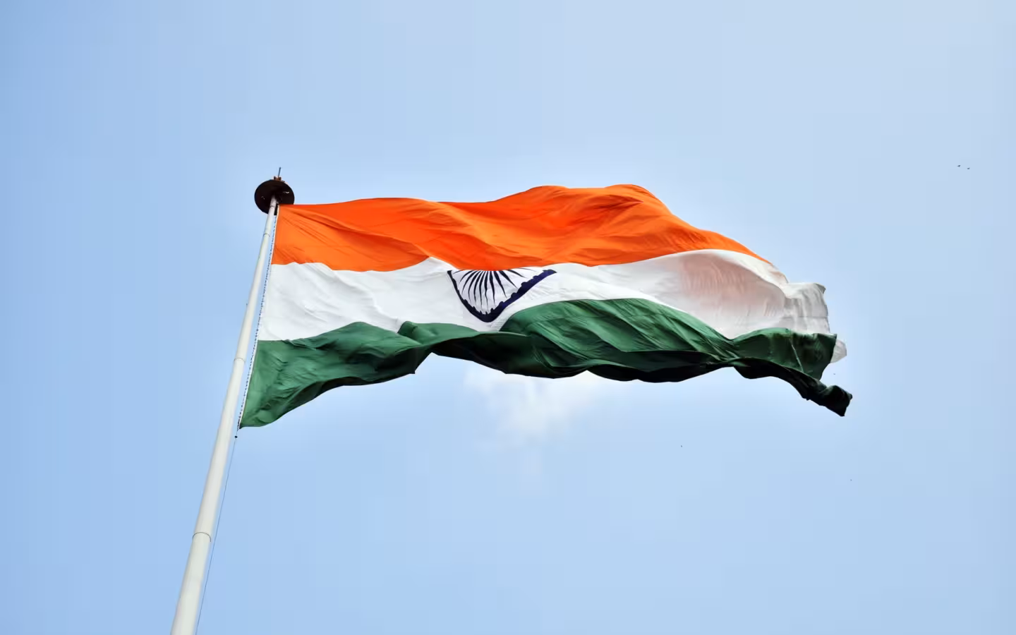 The Indian national flag waves on a pole against a clear blue sky.