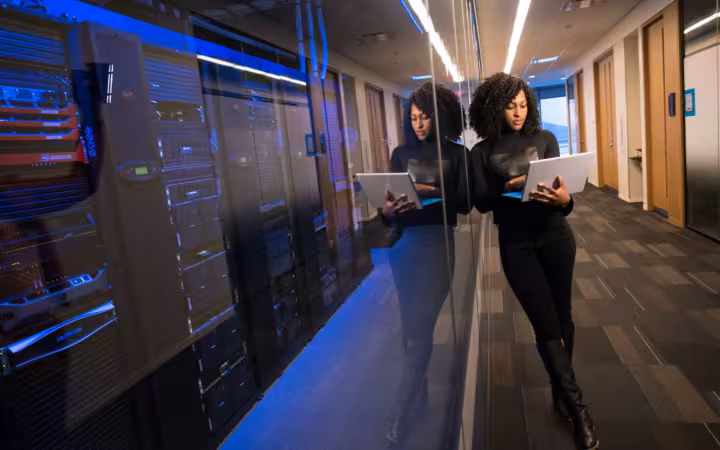 A woman using a laptop beside mirrored server racks in a data center