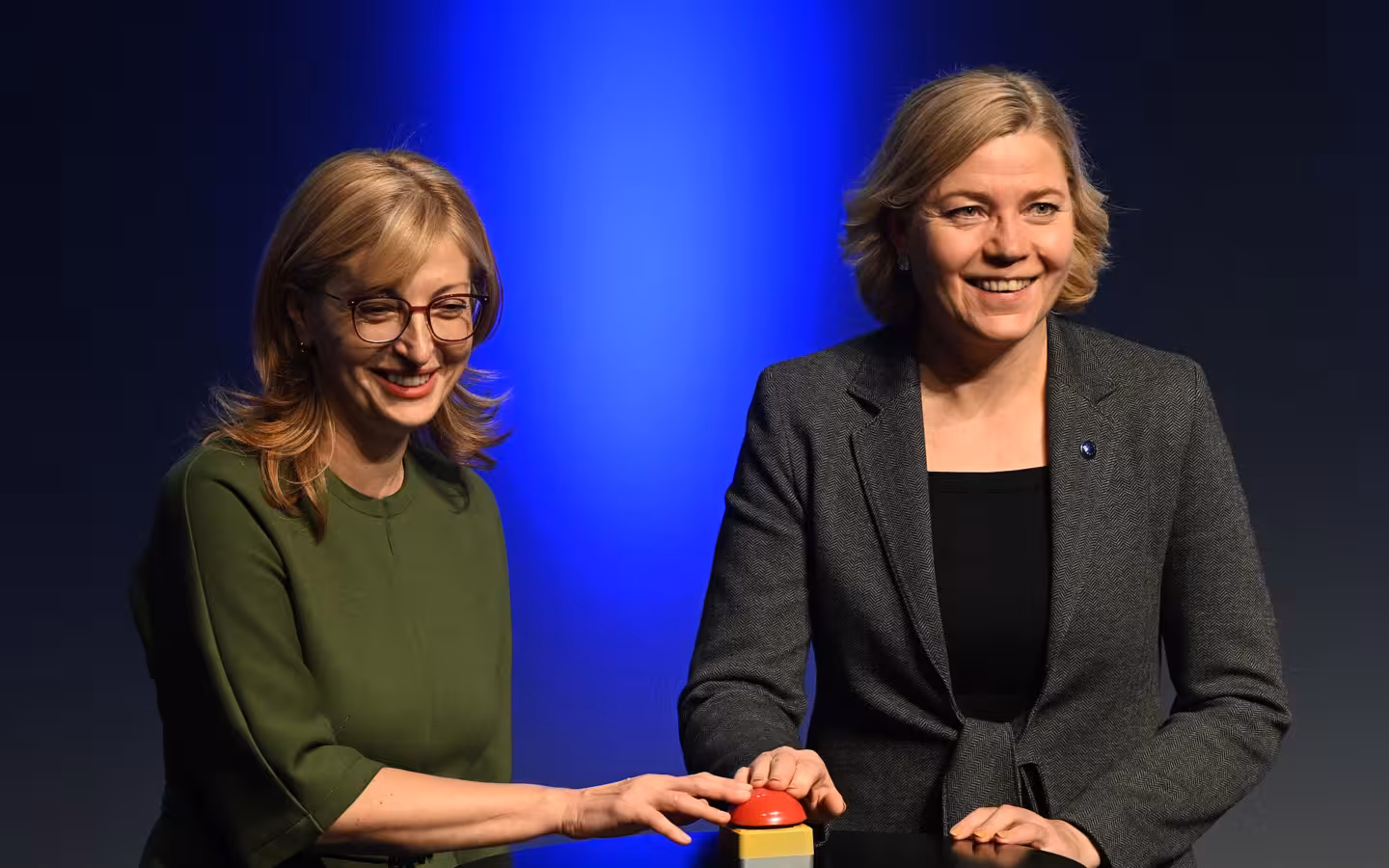 Henna Virkkunen and Ekaterina Zaharieva smile beside a button onstage.
