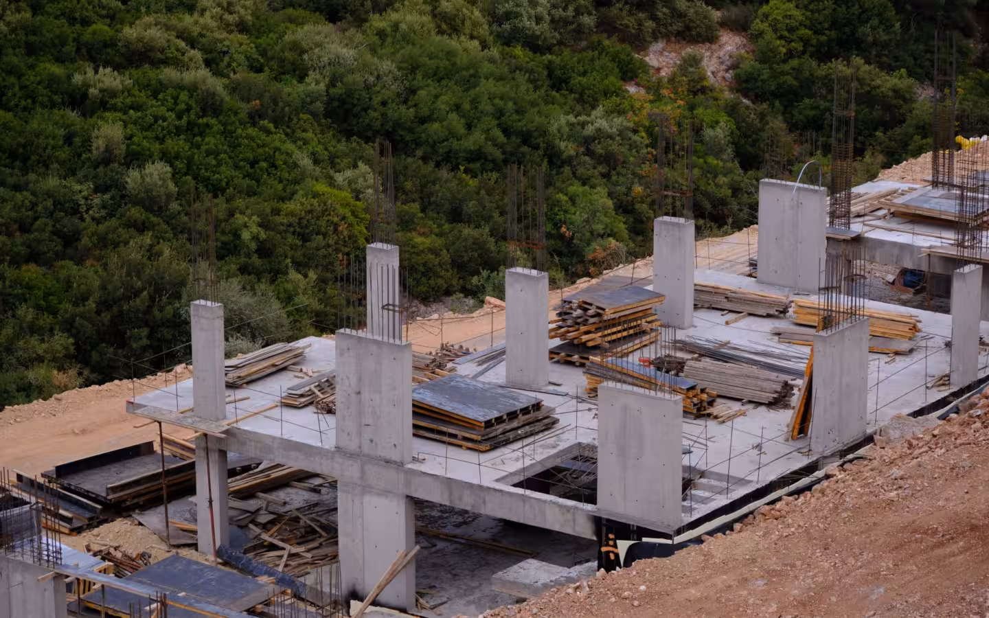 A concrete building framework under construction beside dense green woodland