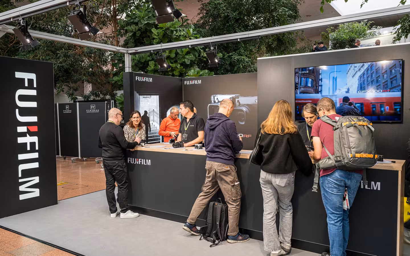 Visitors gather at a Fujifilm booth beneath prominent branding and a display screen.