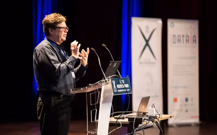 Yann LeCun speaks at an École Polytechnique lectern beside laptops and banners.