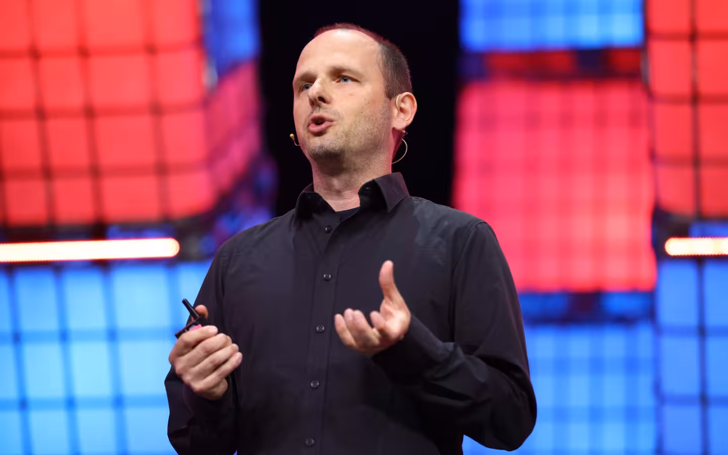 Thomas Dohmke speaks onstage against colorful illuminated panels.