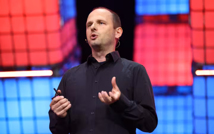 Thomas Dohmke speaks onstage against colorful illuminated panels.