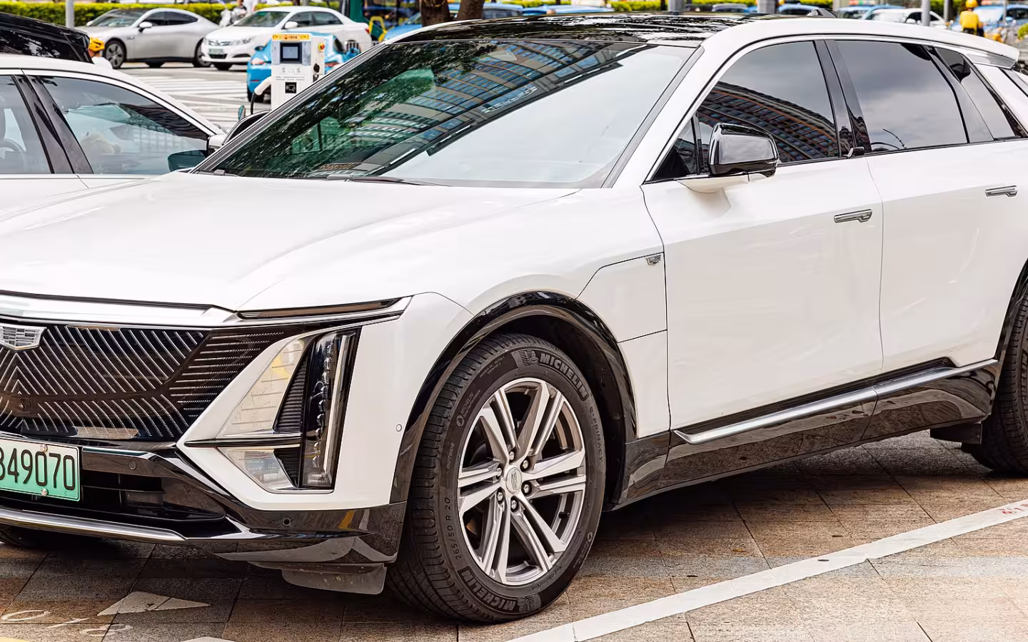 A white Cadillac Lyriq parked outdoors beside other cars.