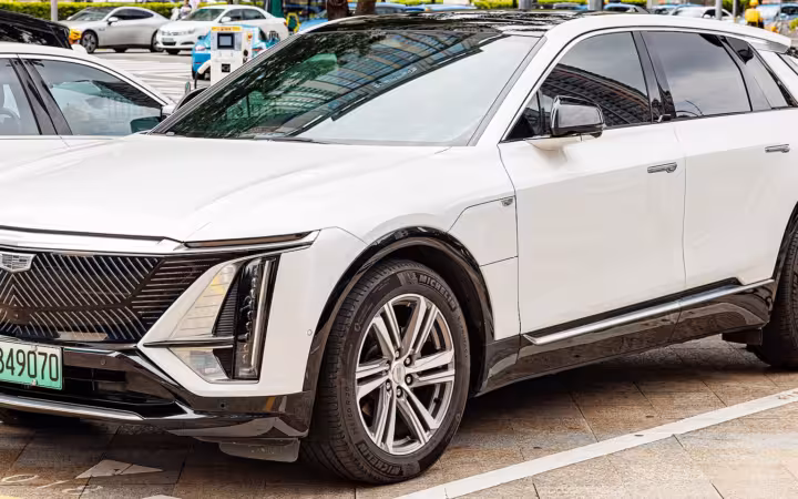 A white Cadillac Lyriq parked outdoors beside other cars.