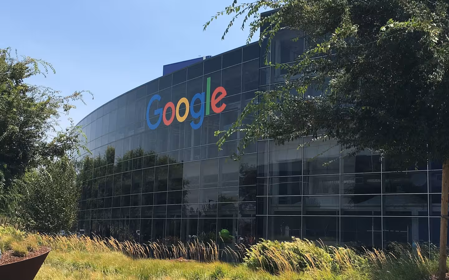 Googleplex Headquarters glass facade with Google logo, trees and foreground grasses