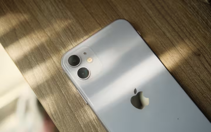 A close-up view of a smartphone with a dual-camera setup placed on a wooden surface, illuminated by soft lighting.