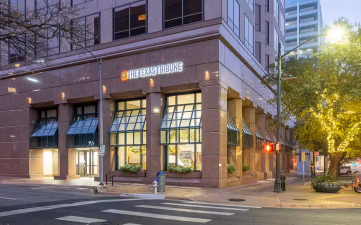 The Texas Tribune sign on an office building along an Austin street at dusk