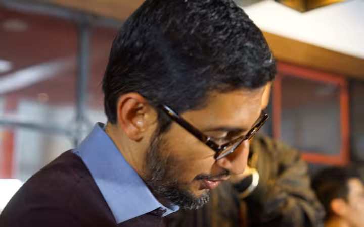 Google CEO Sundar Pichai looks down, with other people behind him.