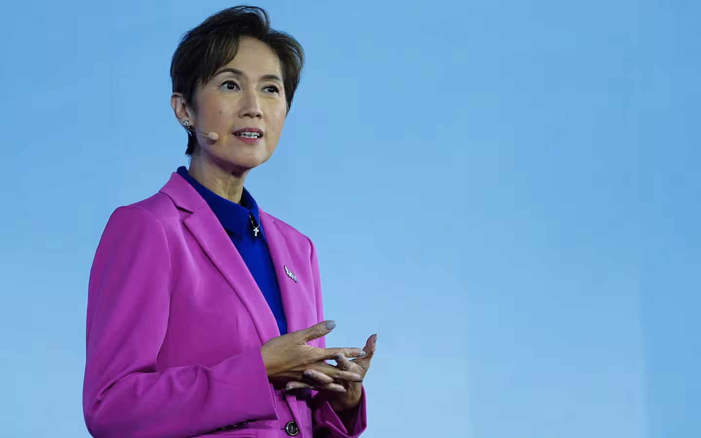 Josephine Teo speaking with a headset microphone against a blue backdrop