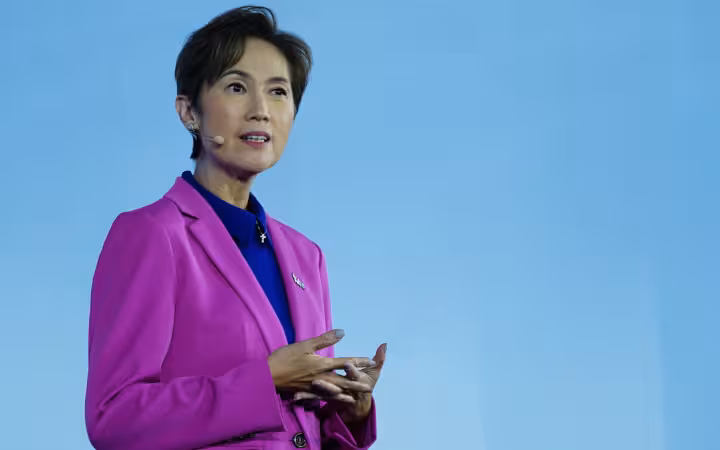 Josephine Teo speaking with a headset microphone against a blue backdrop