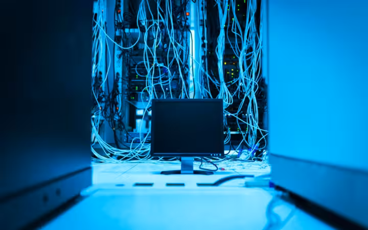 A complex network of cables in a data center with a monitor in the foreground.