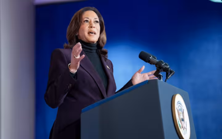 Kamala Harris gestures while speaking at a lectern against a blue backdrop.