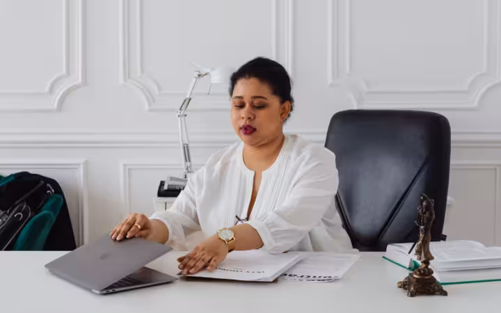 A woman at an office desk opens a laptop beside legal documents.