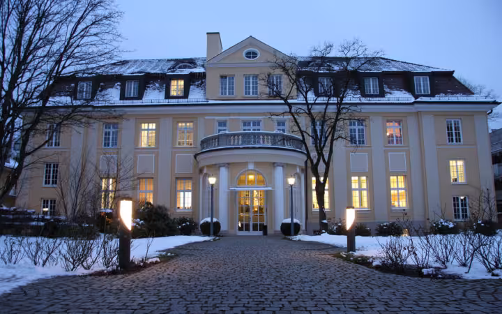 The ifo Institute’s snow-covered main building glows at dusk behind bare trees.