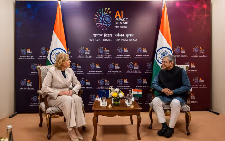 Ashwini Vaishnaw and Henna Virkkunen seated before AI Impact Summit signage and Indian flags