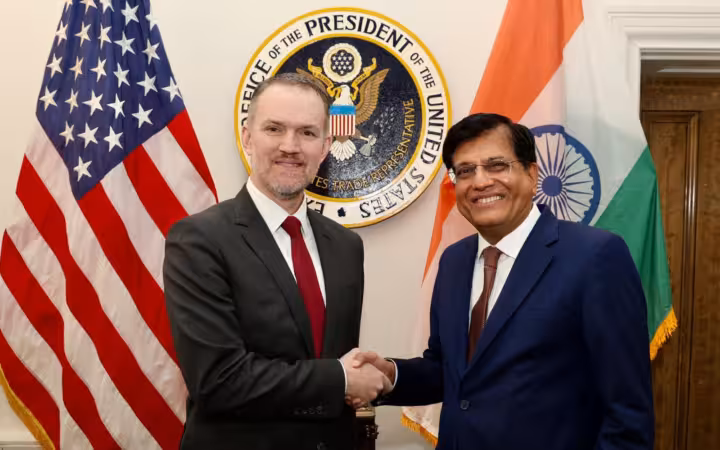 Piyush Goyal and Jamieson Greer shake hands beside U.S. and Indian flags