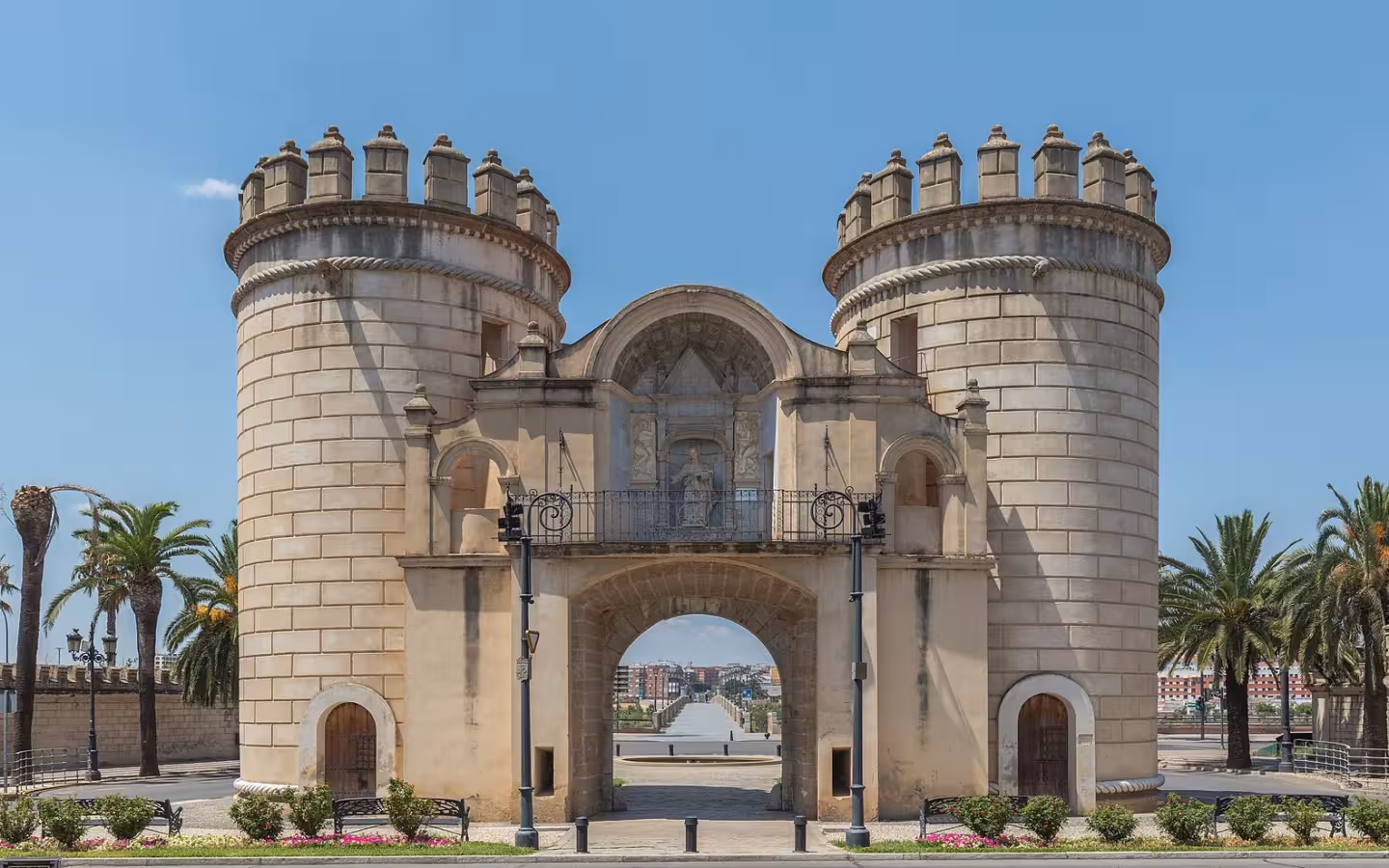 Palmas Gate in Badajoz stands between palm trees beneath a clear sky.