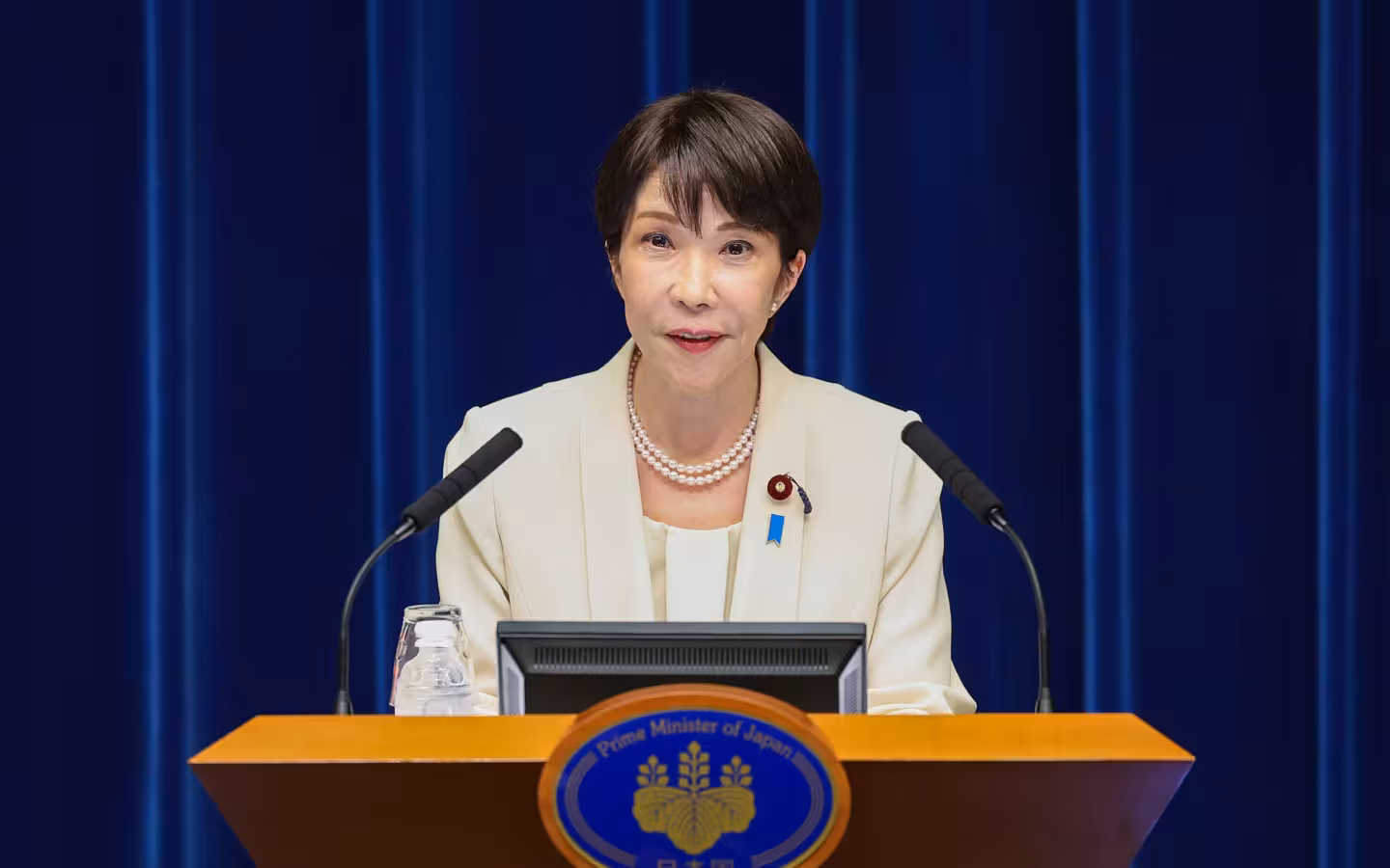 Sanae Takaichi speaks behind a lectern at a press conference.