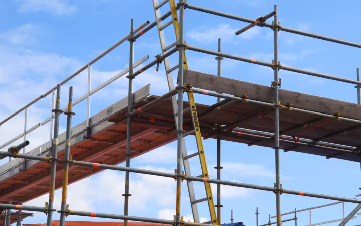 Detailed view of a construction site scaffolding structure and ladder against a bright blue sky.