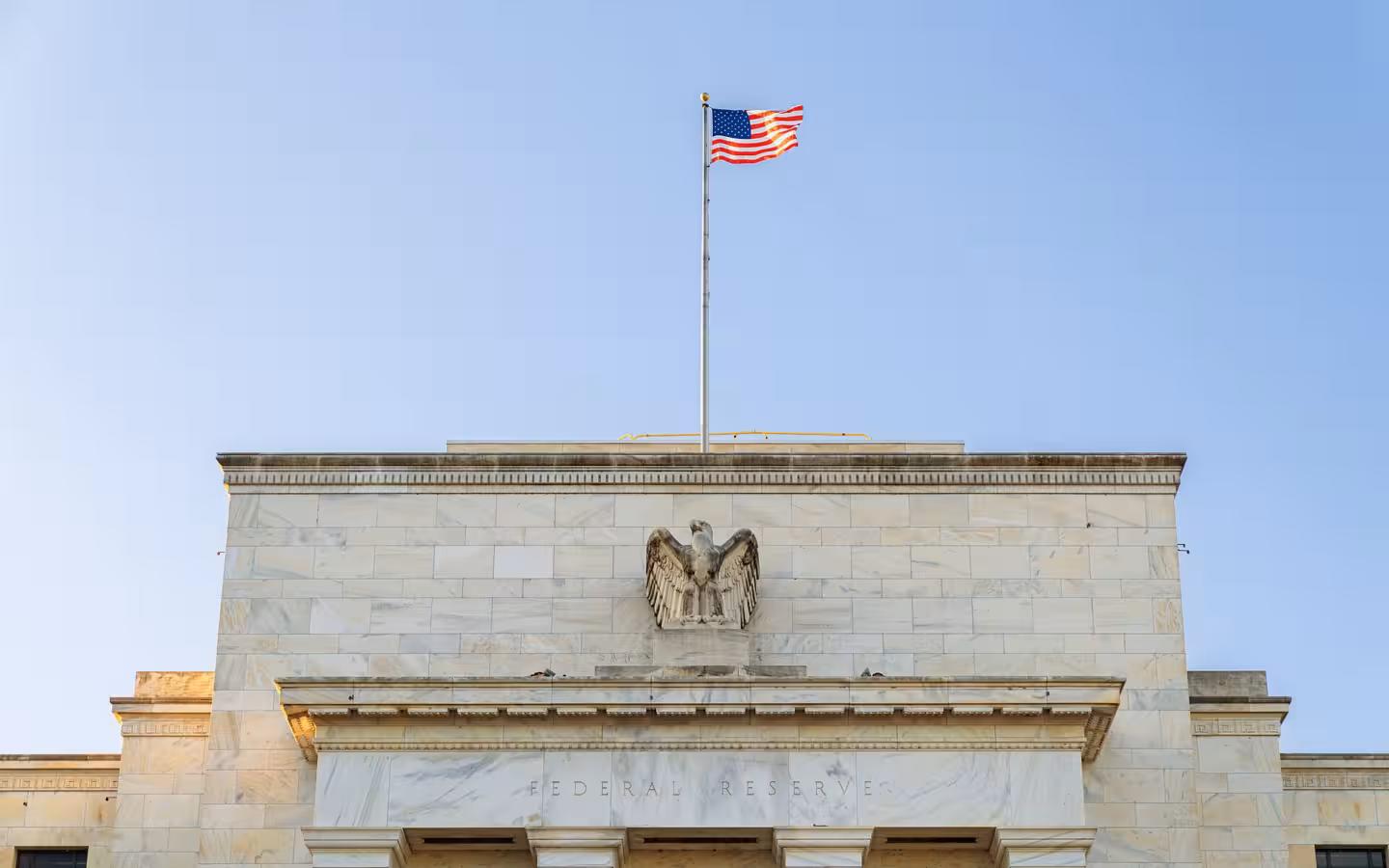 The Federal Reserve building facade beneath an American flag in Washington, D.C.