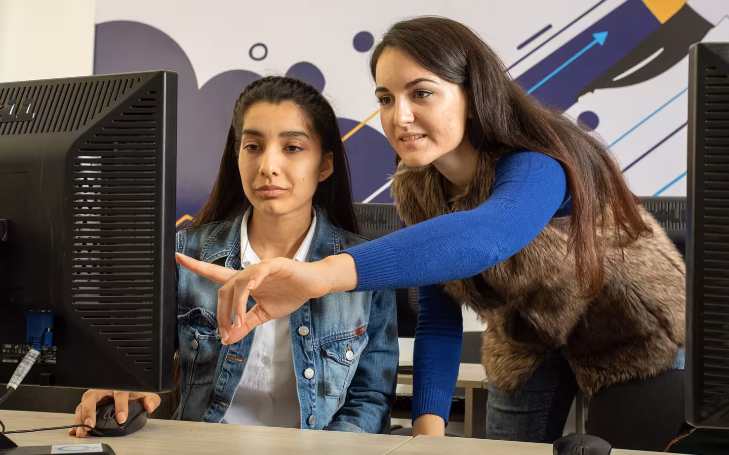 A trainer points at a monitor while a data annotator works.