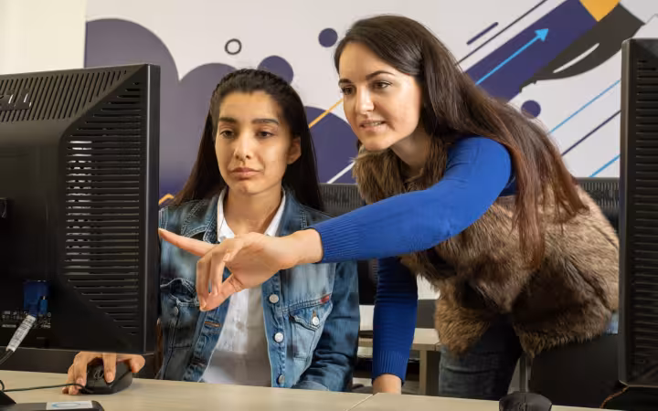 A trainer points at a monitor while a data annotator works.