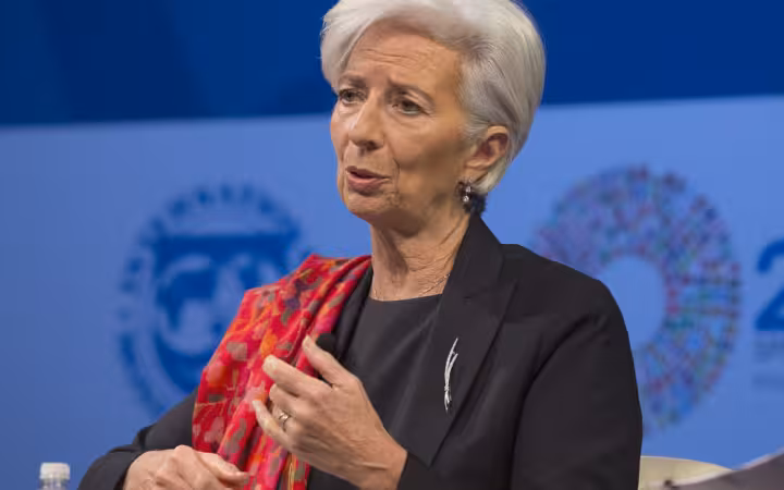 Christine Lagarde speaking and gesturing against a blue conference backdrop.