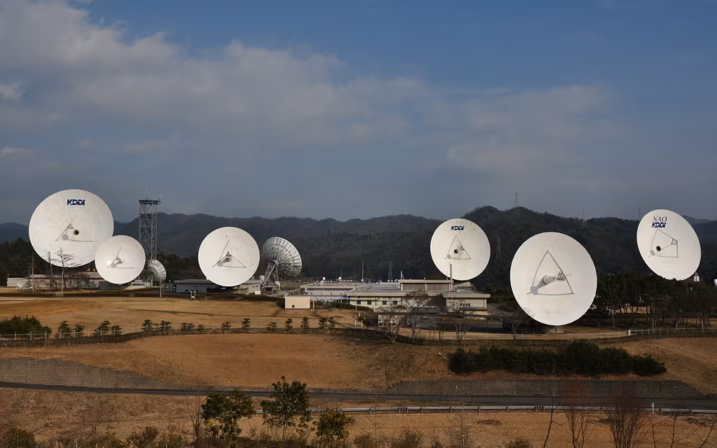 Several large satellite dishes at KDDI’s Yamaguchi Satellite Earth Station beneath a cloudy sky