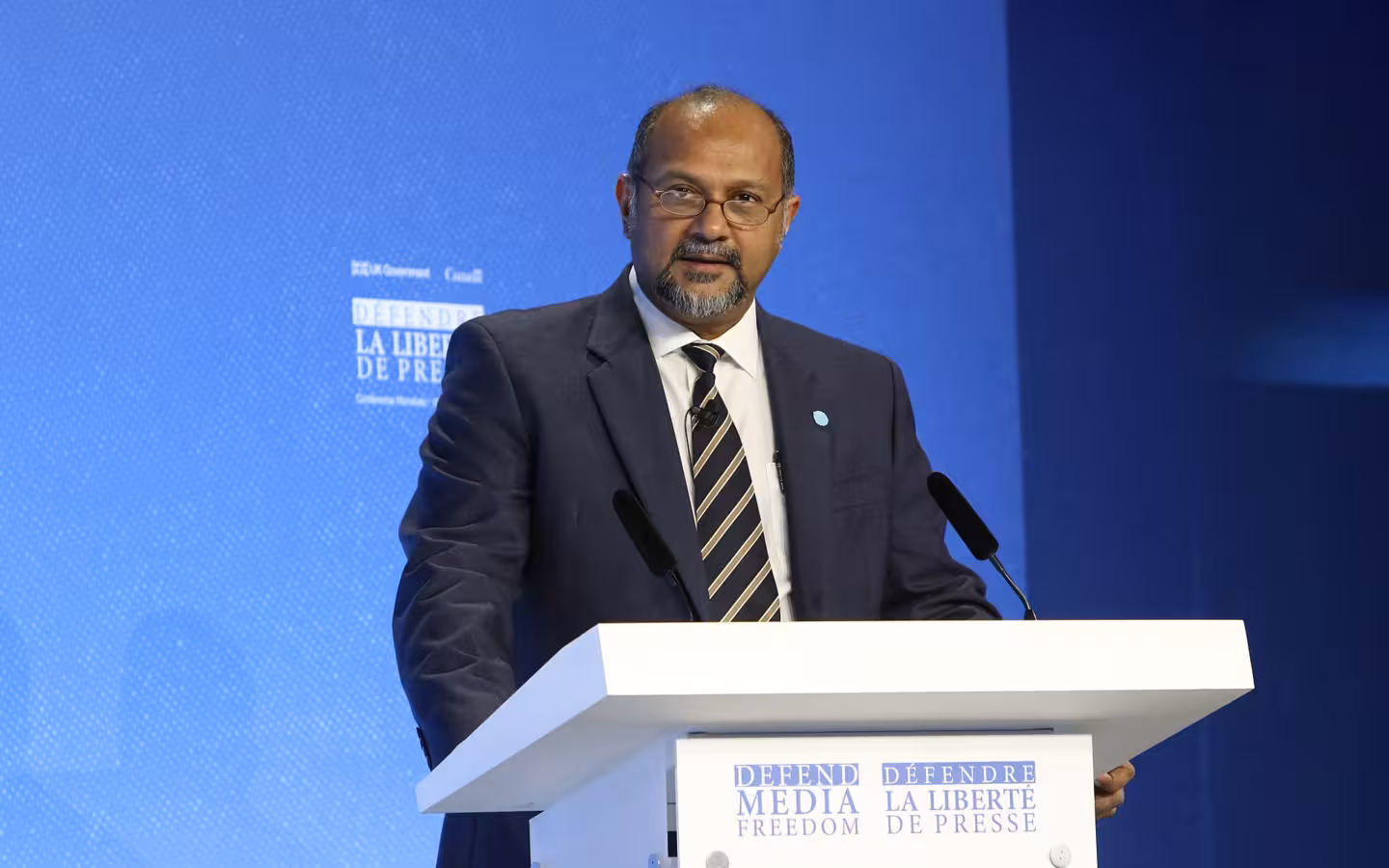 Gobind Singh Deo speaking at a lectern against a blue conference backdrop