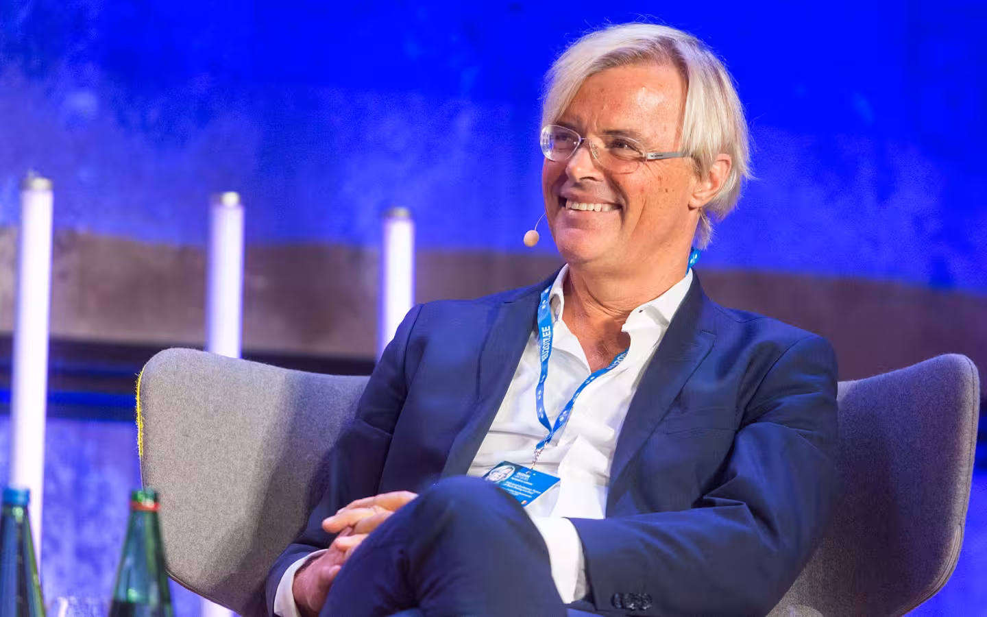 Jacques Bughin seated and smiling onstage, wearing a suit and headset microphone