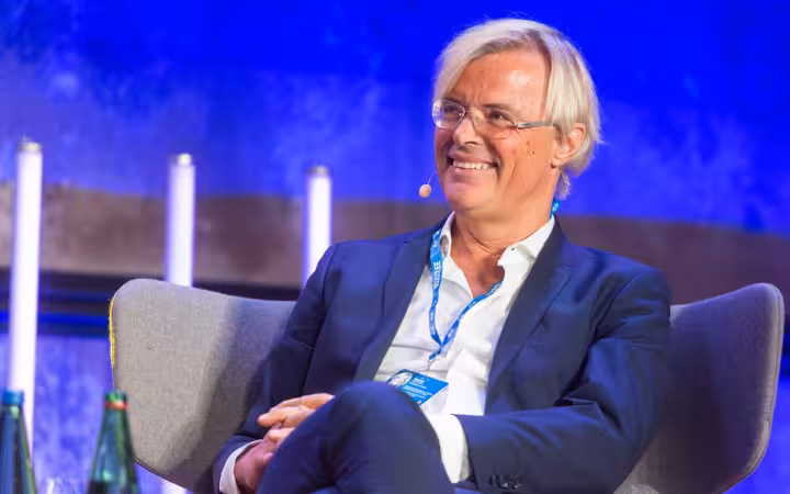Jacques Bughin seated and smiling onstage, wearing a suit and headset microphone