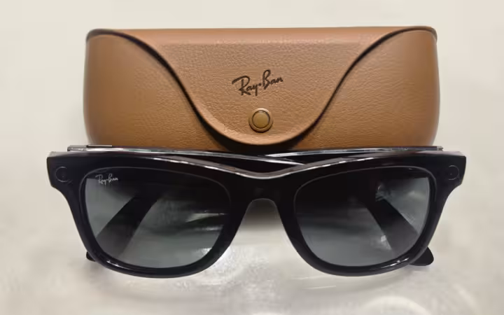 Black Ray-Ban Meta smart glasses sit in front of a brown charging case.