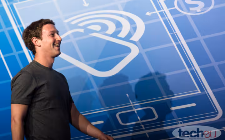 Mark Zuckerberg smiling in profile before a blue mobile-themed backdrop.